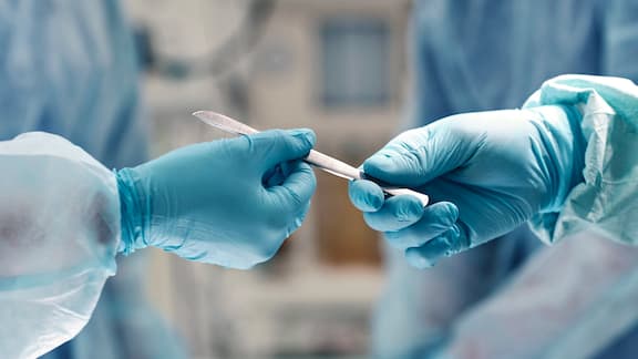 A picture of two hands clad in surgical gloves and reaching for an instrument.