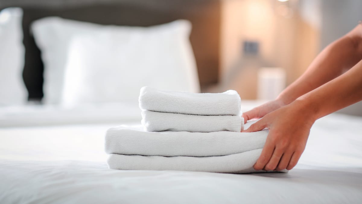 Händer viker handdukar på säng.