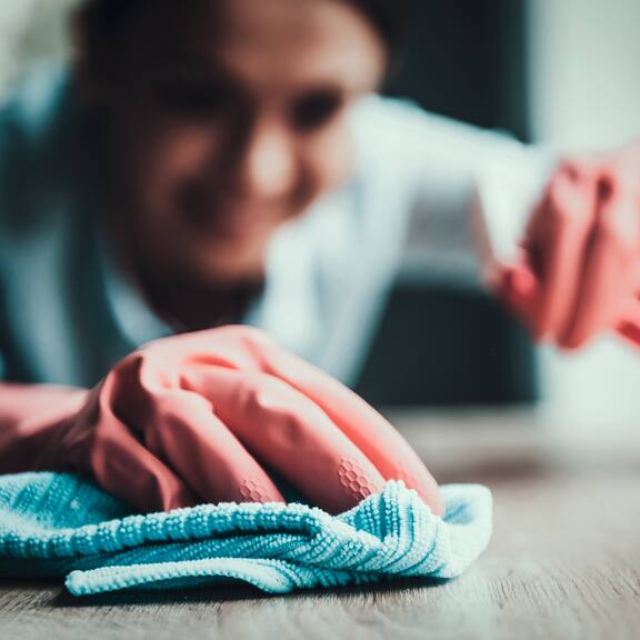 Una persona che indossa guanti di gomma pulisce una superficie con un panno per la pulizia.