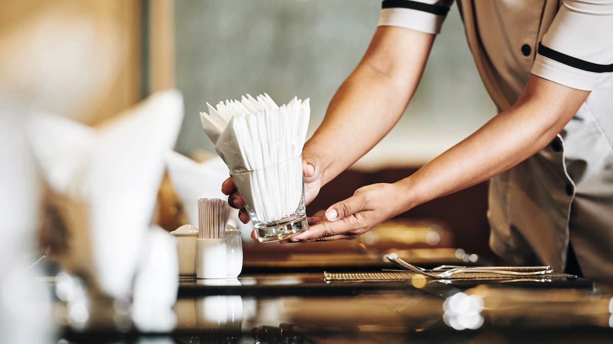 Unas manos montan una mesa con servilletas en el restaurante.