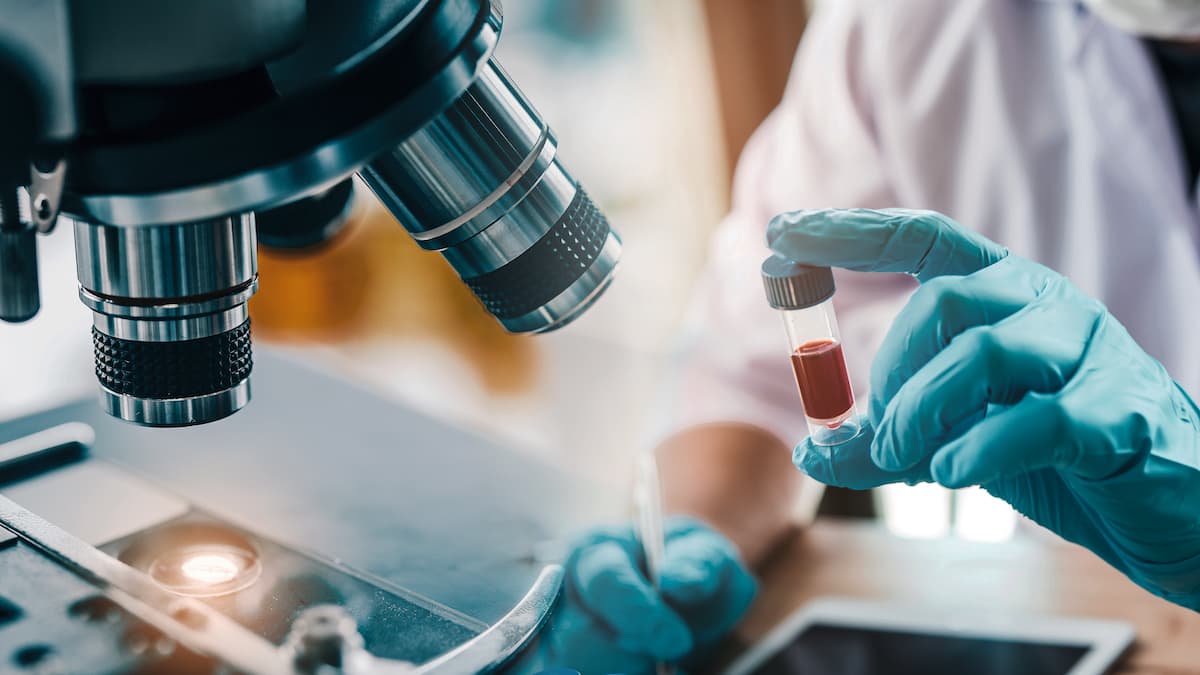 Hand holds a sample of red liquid.