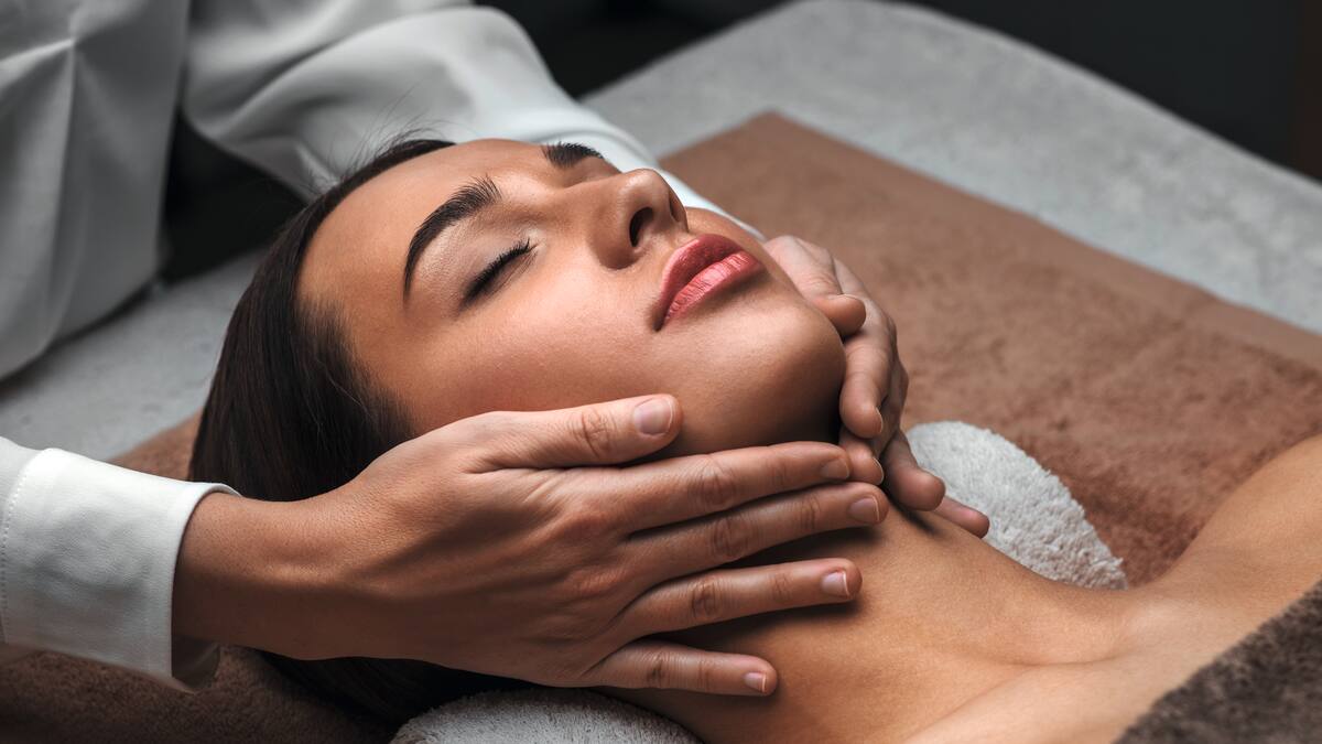 Handen masseren het gezicht van een vrouwelijke klant.