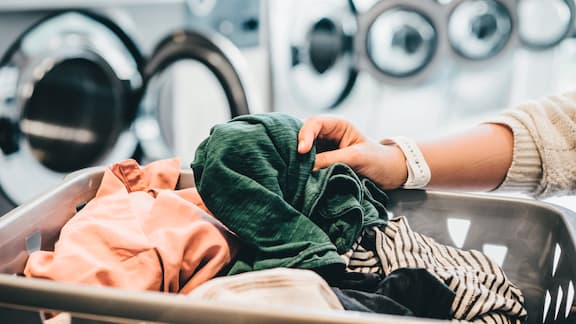 Una mano tocca vestiti di bucato dentro una cesta di plastica in una lavanderia comune