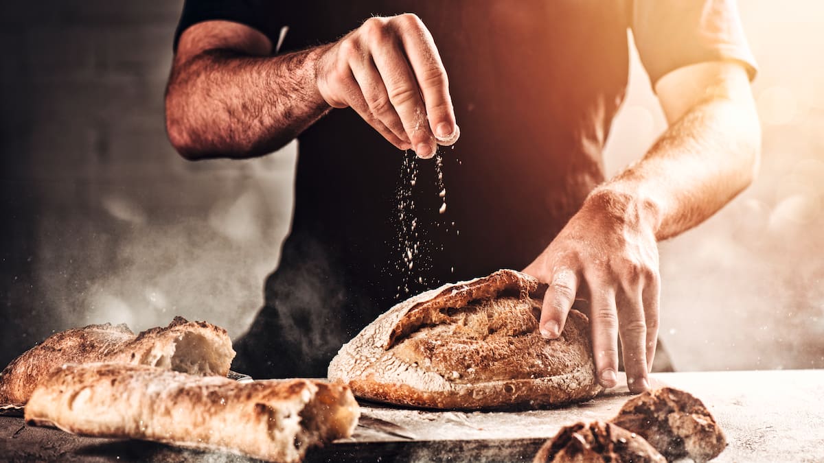 Un boulanger saupoudre le pain de farine.