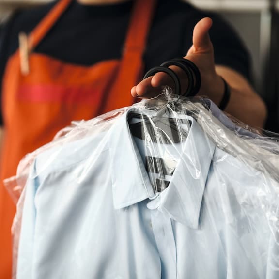 A hand is presenting freshly cleaned shirts covered in protective film.