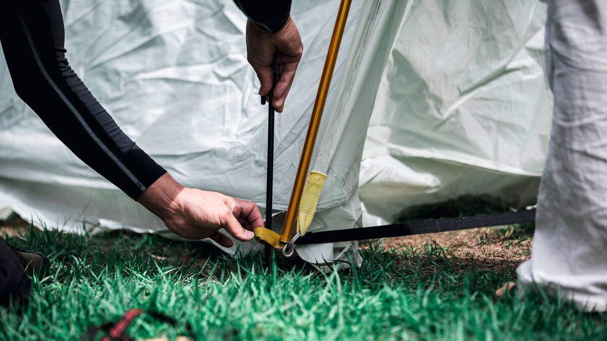 Hands secure a tent in the grass.