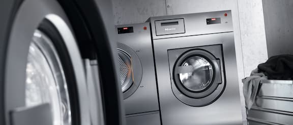 Pakkebilde av mørke Miele Professional vaskemaskiner med sølvfarget vaskekurv.