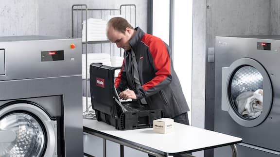 Un technicien de service de Miele répare un appareil avec des pièces de rechange.