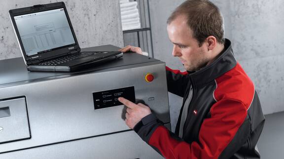 Miele service technician stands with laptop at commercial washing machine.