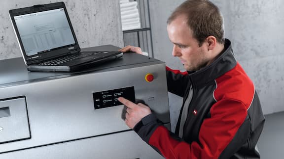 Miele service technician stands with laptop at commercial washing machine.