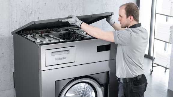Técnico do serviço de assistência técnica abre o tampo de uma máquina de lavar roupa industrial Miele Professional