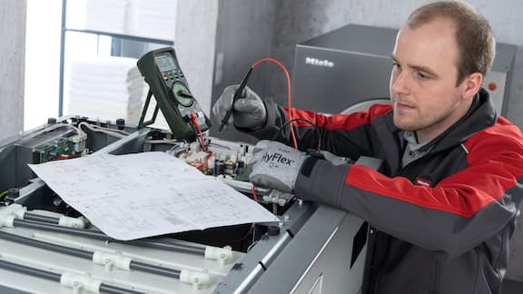 Un technicien de service Miele Professional tient un appareil de mesure dans la main et vérifie une machine professionnelle