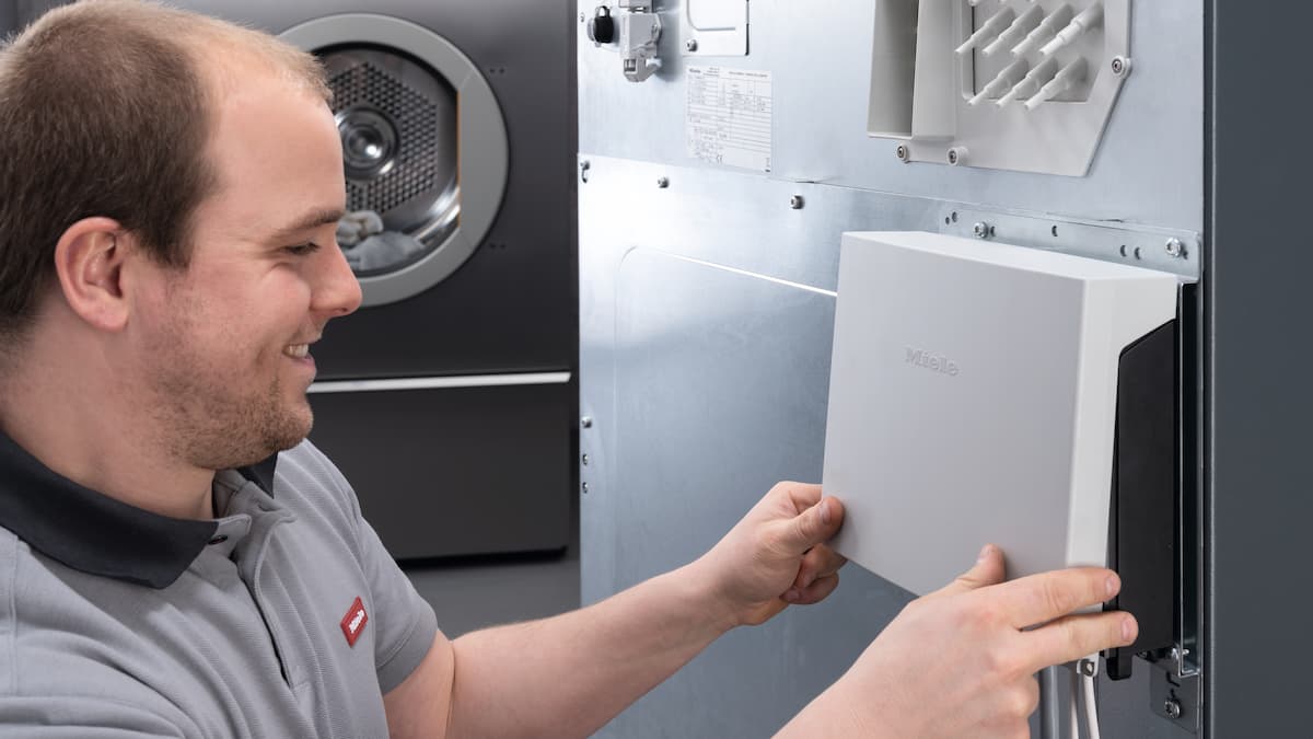 Service technician installs spare part on back of Miele Professional commercial washing machine