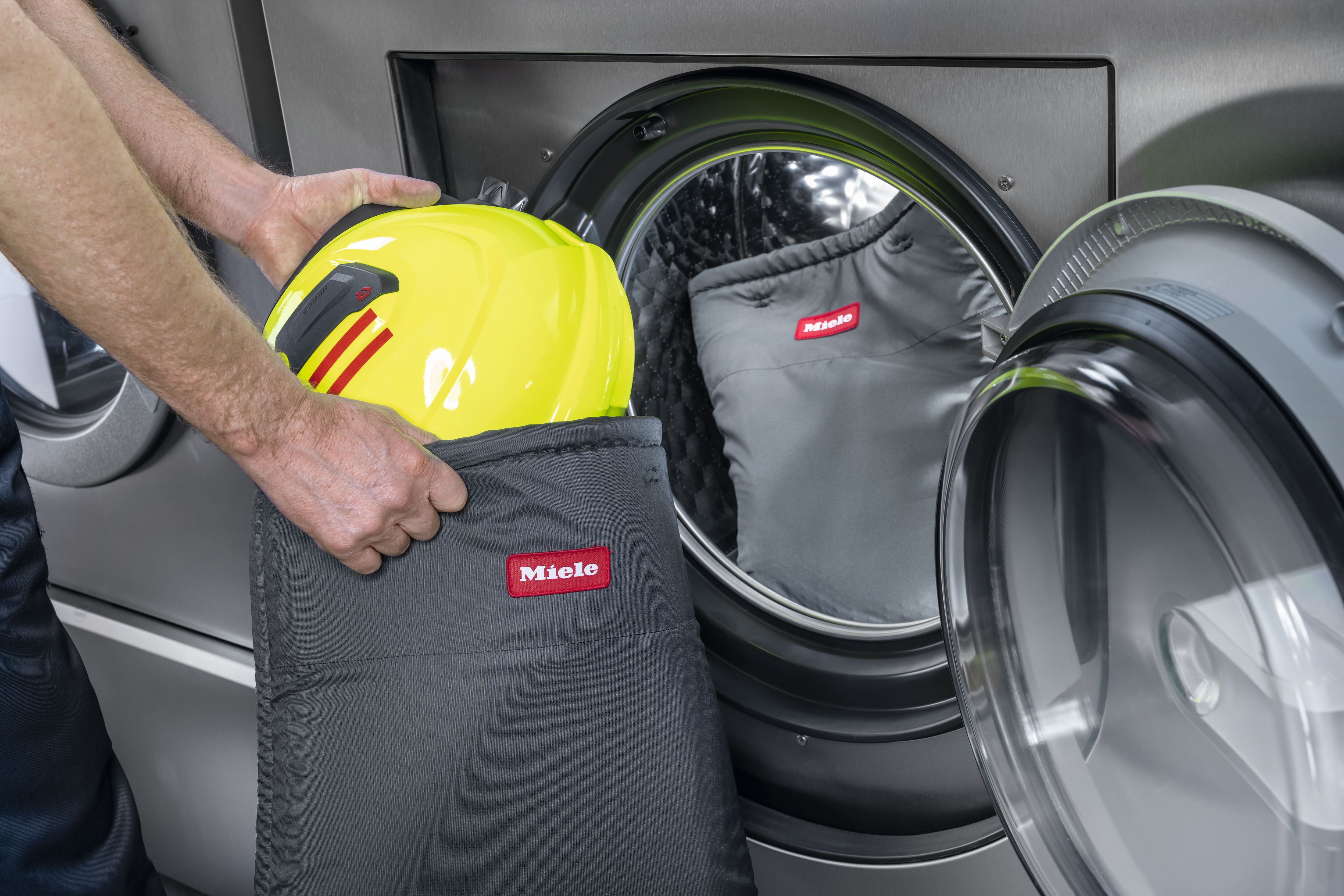 Eine Person verstaut einen Helmes in einen dafür vorgesehen Miele Professional Waschsackes, bevor dieser in die Waschmaschine gelegt wird