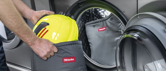 A person stows a helmet in a Miele Professional laundry bag provided for this purpose before placing it in the washing machine