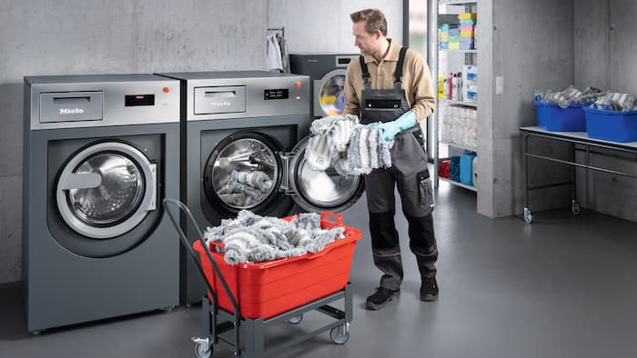 A contract cleaner loads a Miele Professional washing machine with mops.