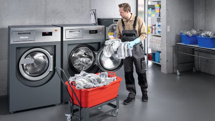 Een medewerker van de gebouwenreiniging stopt mops in een wasmachine van Miele Professional.