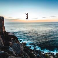 Slackliner is balancing on a rope between two peaks with the sea in the background.