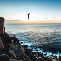 Slackliner is balancing on a rope between two peaks with the sea in the background.