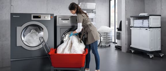 Service employee clears white laundry from an industrial washing machine from Miele Professional
