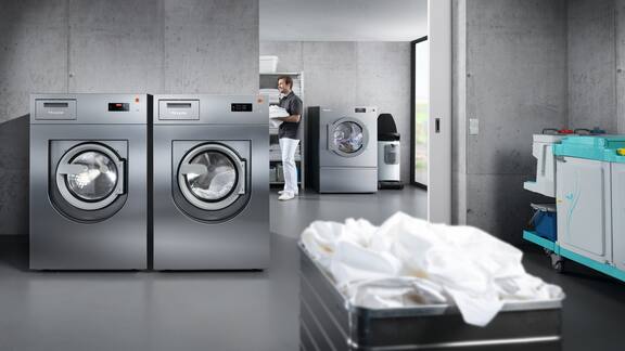 Un lave-linge et un sèche-linge gris, situés dans une laverie à l’aspect béton.