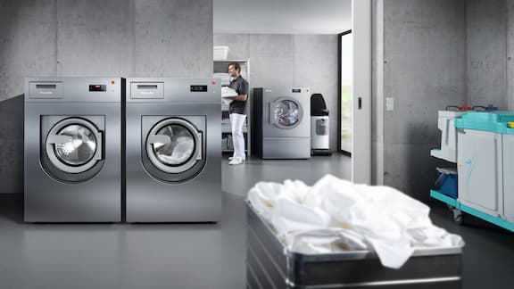 En grå vaskemaskine og tørretumbler er placeret i et vaskeri med betonudseende.