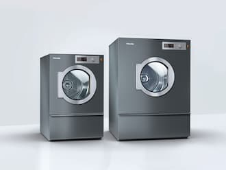 Two Miele tumble dryers stand in a white room