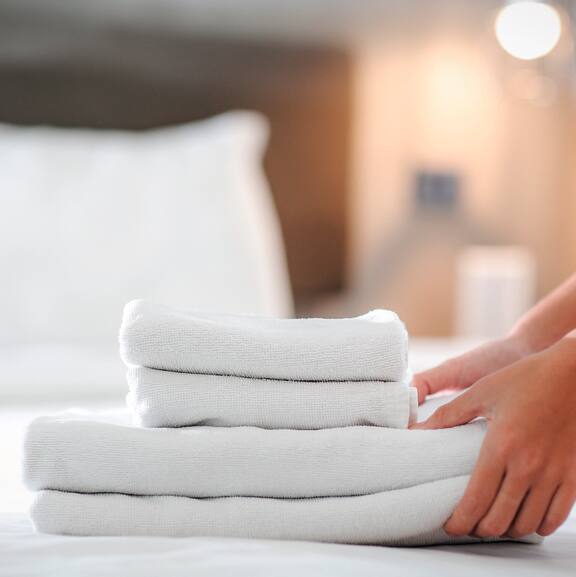 Toalhas brancas acabadas de lavar são colocadas sobre uma cama de hotel.
