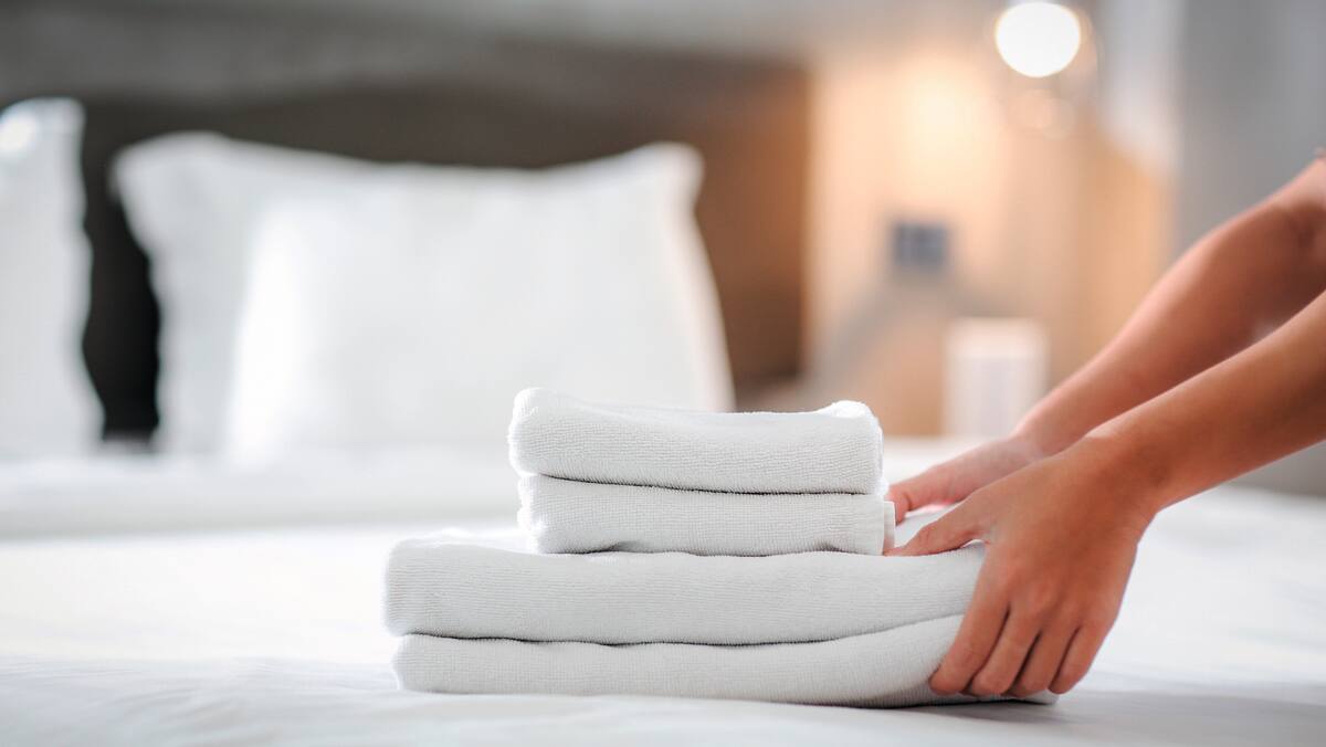 Frisch gewaschene weisse Handtücher werden auf ein Hotelbett gelegt