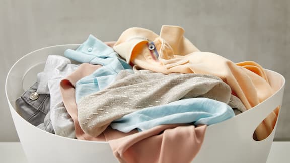Iso pyykkikori täynnä erilaisia puhtaita tekstiilejä.