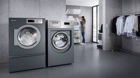 Grijze wasserijruimte met wasmachine en droogkast en kleding die aan een stang hangt.