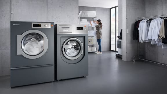 Grijze wasserijruimte met wasmachine en droger en kleding die aan een stang hangt.