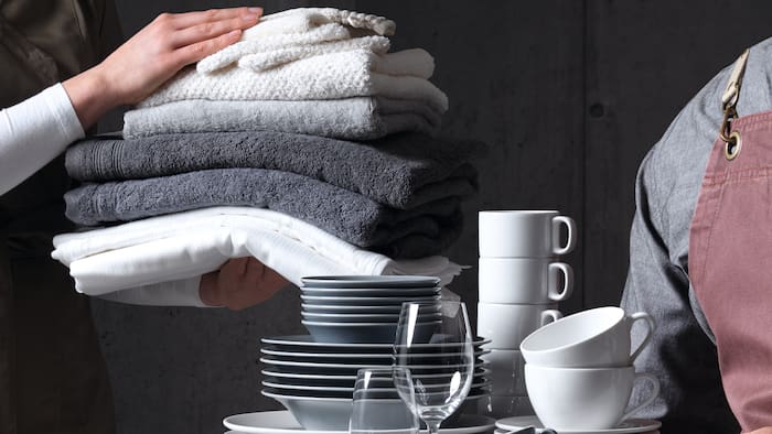 Gros plan sur deux personnes tenant une pile de vaisselle et une pile de serviettes
