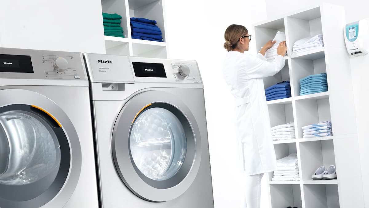Primo piano sulle lavatrici professionali e donna con camice bianco sullo sfondo