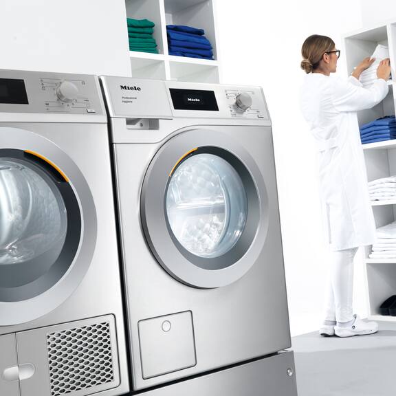 Kuva huoneesta, jossa on pyykinpesukone, kuivausrumpu ja laboratorioteknikko lajittelemassa pyykkiä