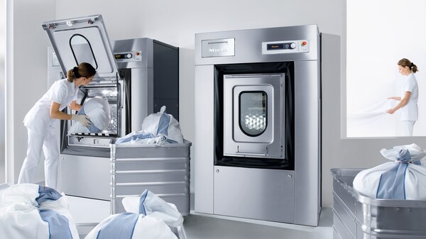 Wäschereikraft befüllt Miele Professional Gewerbewaschmaschinen in Inhouse-Wäscherei mit Wäschesacken