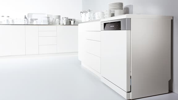 White kitchenette with integrated white dishwasher and crockery on the work surface.