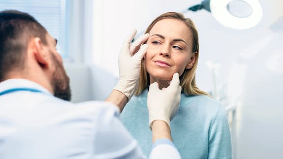 Un dermatologue examine la peau au niveau de l’œil d’une femme.
