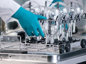 Duas mãos com luvas de borracha levantam a vidraria de laboratório de uma máquina de lavar e desinfetar para laboratório