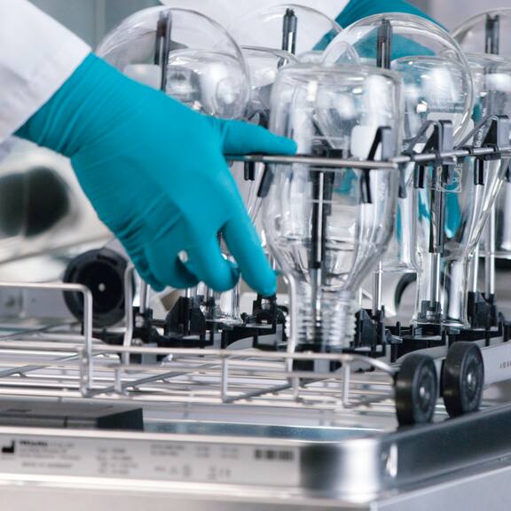 Une main fait glisser un module SimpleLoad dans un laveur de laboratoire – rempli de différentes pièces de verrerie de laboratoire.