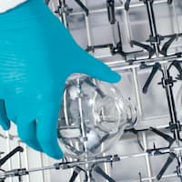 A hand places a laboratory glass in an injector module.