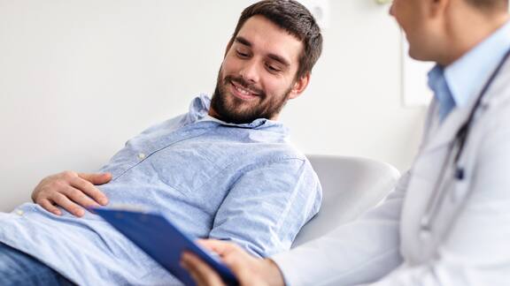 A man on a surgery bed holds his stomach and is in a consultation with a doctor.