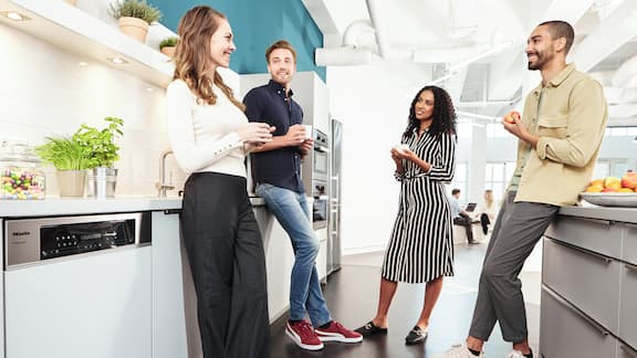 Μια παρέα συναδέλφων απεικονίζονται να στέκονται στον χώρο της μίνι κουζίνας όπου συζητούν πίνοντας καφέ.