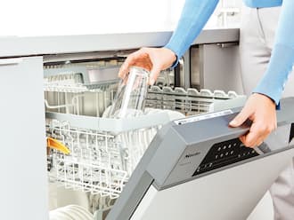 A person is stacking glasses in a Miele dishwasher