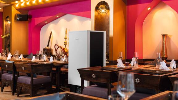 A Miele AirControl purifier is positioned between the laid tables and chairs at the restaurant.