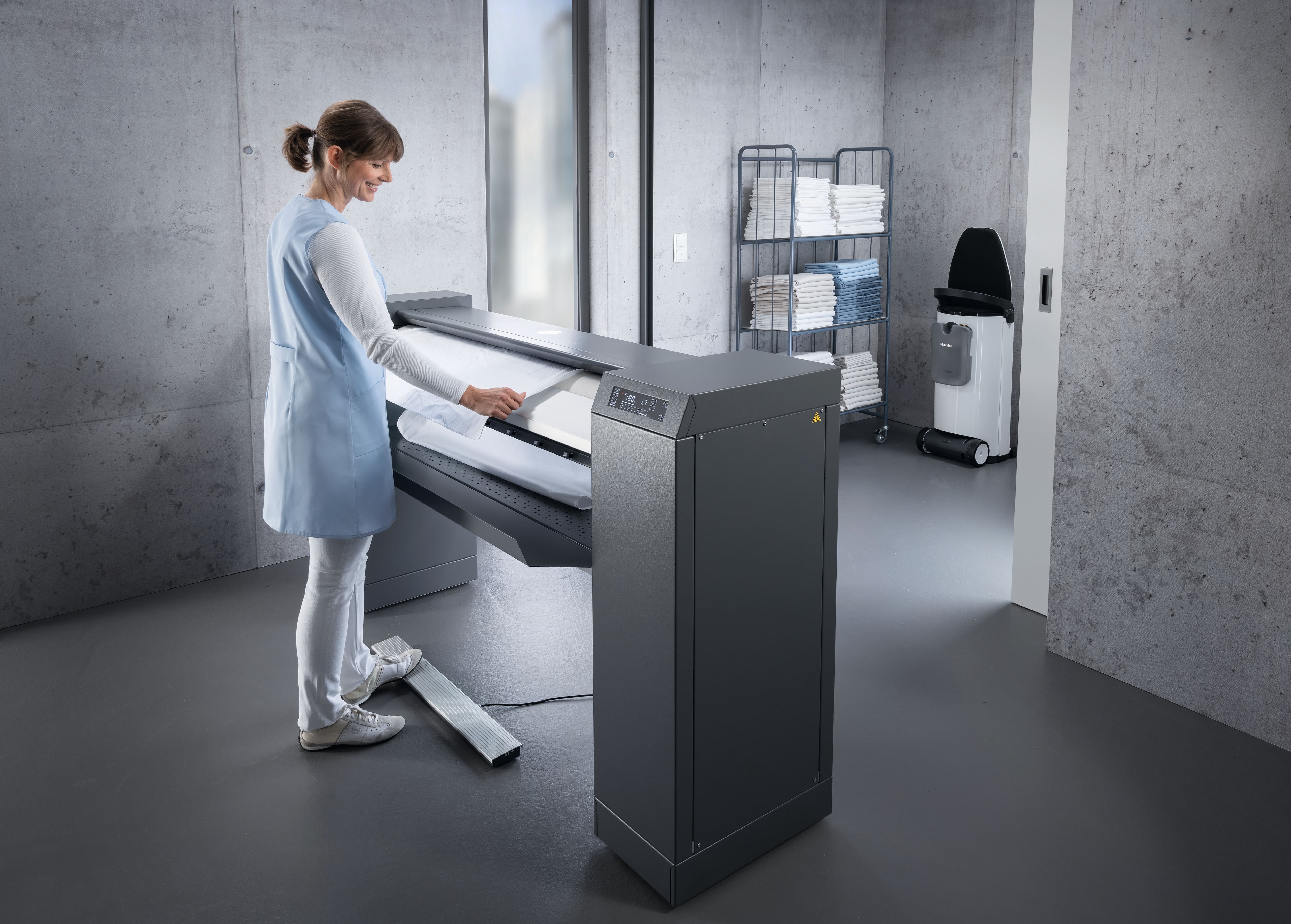 A woman in a laundry operating a rotary ironer.
