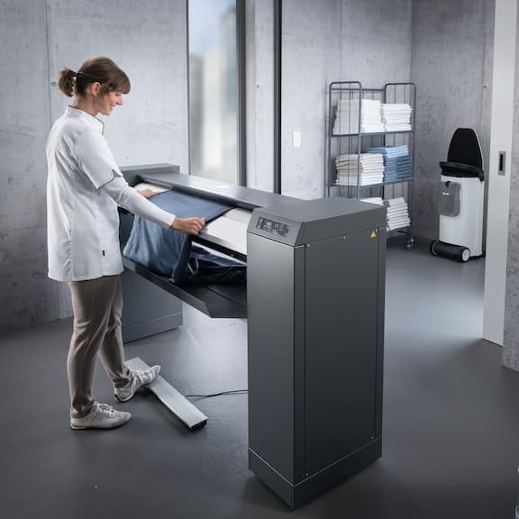 A laundry room worker is using the Miele flat ironer PRI 214.