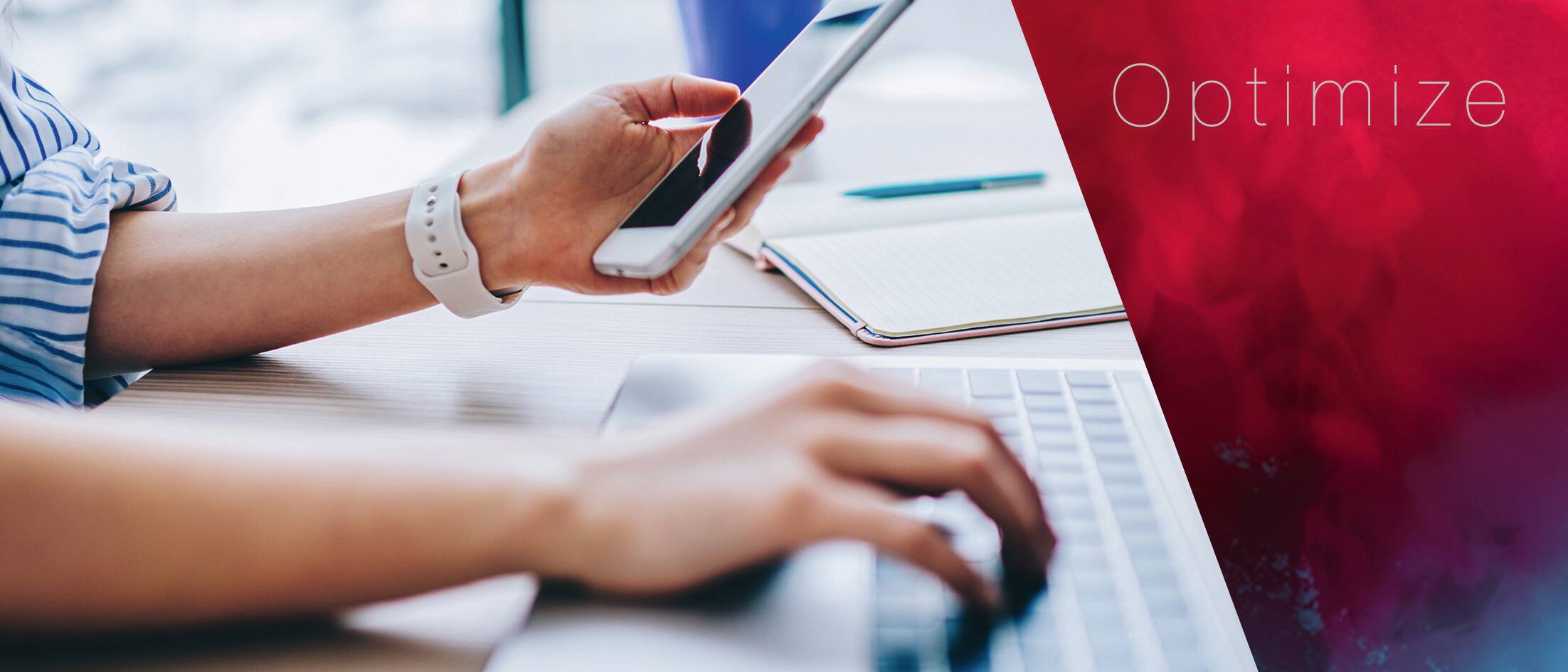 Person arbeitet am Laptop und hat ein Smartphone in der Hand