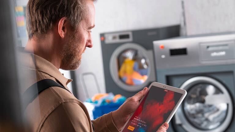 Een man in bedrijfskleding gebruikt een tablet in de buurt van wasmachines