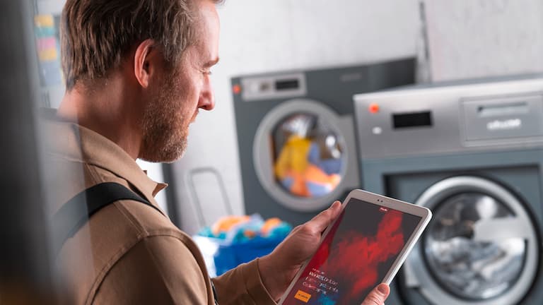Ein Mann in Arbeitskleidung nutzt ein Tablet im Umfeld von Waschmaschinen